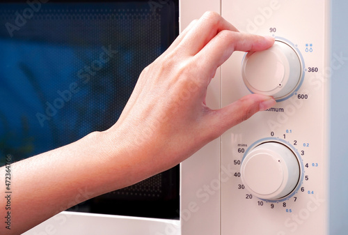 Woman's hand adjusts the temperature with a circular button to warm food from the kitchen microwave.                          