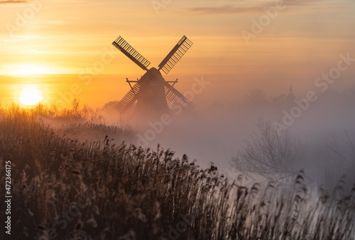 Dutch sunrise with traditional windmill and a canal in the spring fog.
