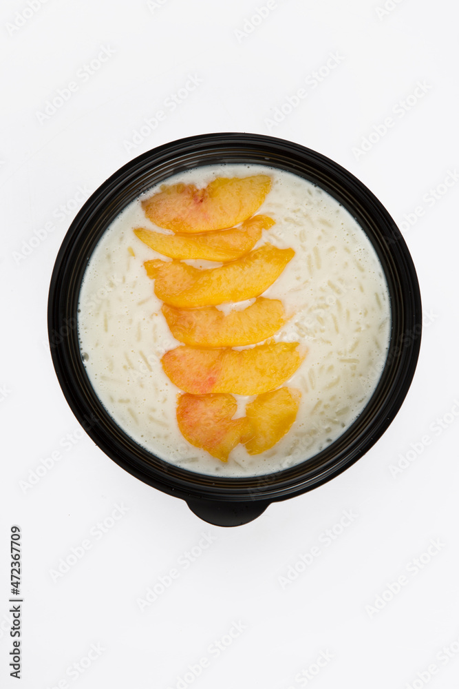 isolated close up top view shot of a delicious white rice milk porridge with peach fruit slices on top in a black plastic bowl on a white background isolated close up top view shot of a delicious white rice milk porridge with peach fruit slices on top in a black plastic bowl on a white background