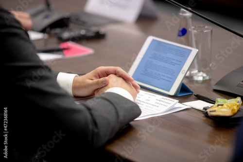 One of politician sitting by table with his hands over document during political summit or conference