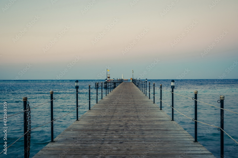 Wooden pier at sunrise in the tropical sea. Palm trees in the distance. Beautiful wooden pier. Long exposure of the sea as a haze