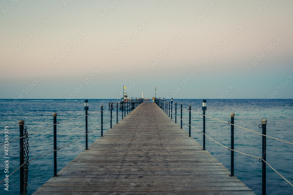 Wooden pier at sunrise in the tropical sea. Palm trees in the distance. Beautiful wooden pier. Long exposure of the sea as a haze