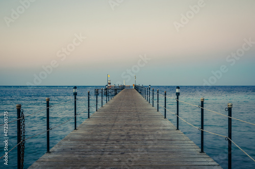 Wooden pier at sunrise in the tropical sea. Palm trees in the distance. Beautiful wooden pier. Long exposure of the sea as a haze