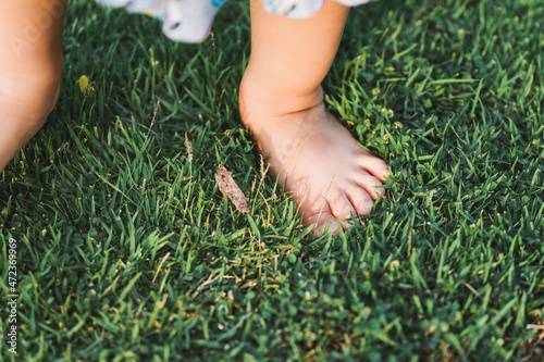 Feet baby child standing on green grass. Girl learn her senses with nature. Kid and sensory concept. © Kanthita
