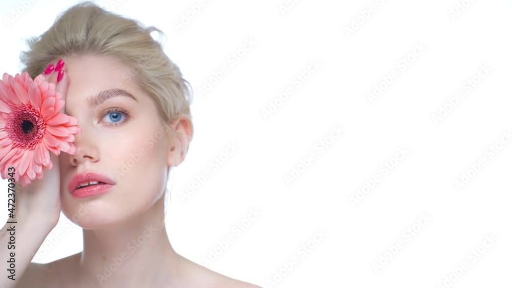 Beautiful young girl with clean skin and pink gerbera in her hand posing at the camera. White background. Beautiful young girl with clean skin and pink gerbera in her hand posing at the camera. White background.