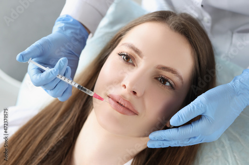 Young woman gets injection of botox in her lips  cosmetologist using syringe