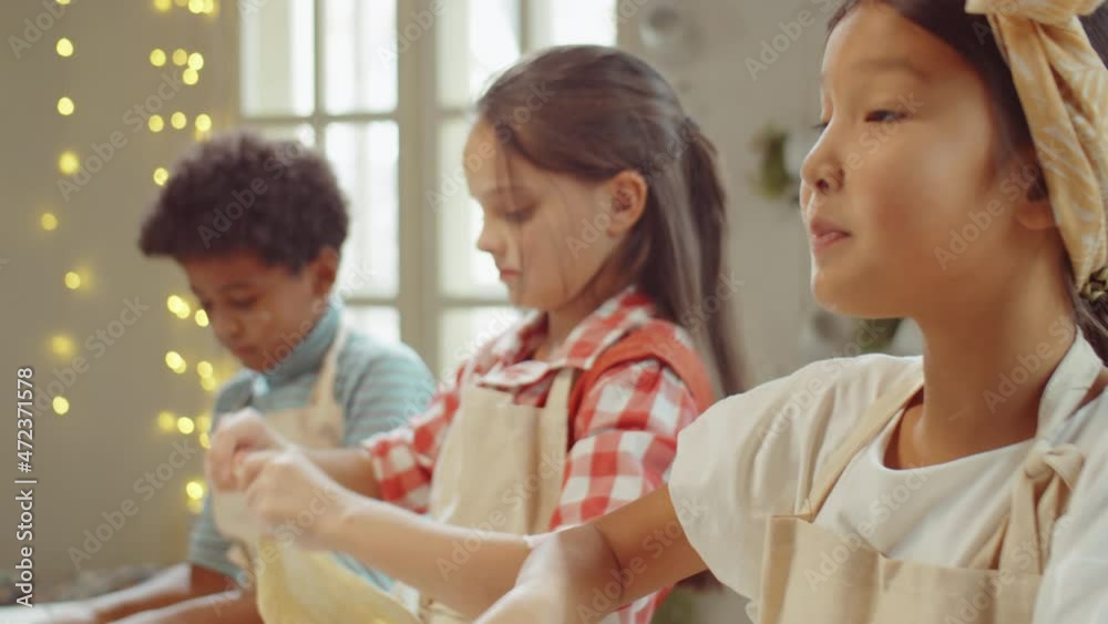 Little Asian girl preparing dough for baking, smiling and telling something during kids cooking class Little Asian girl preparing dough for baking, smiling and telling something during kids cooking class