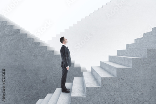 Wall Mural Attractive young european businessman standing on concrete stairs with mock up place