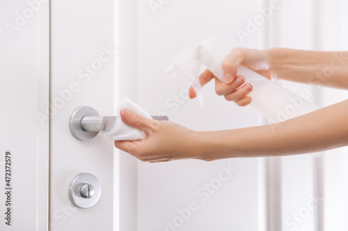 Cleaning white door handles with an antiseptic wet wipe and sanitizer spray. Disinfection in hospital and public spaces against corona virus. Woman hand using towel for cleaning home room door link.
