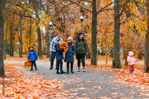 Portrait of a family with children in an autumn city park - happy people walking together, beautiful nature with yellow leaves as background.