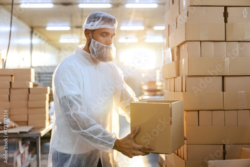 A food factory worker in a white sterile uniform is holding an opened box with cookies and preparing to check quality.
