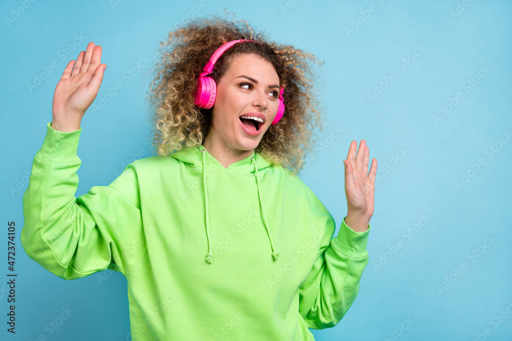 Photo of carefree lady enjoy weekend rest disco wear earphones green hoodie isolated blue color background Photo of carefree lady enjoy weekend rest disco wear earphones green hoodie isolated blue color background