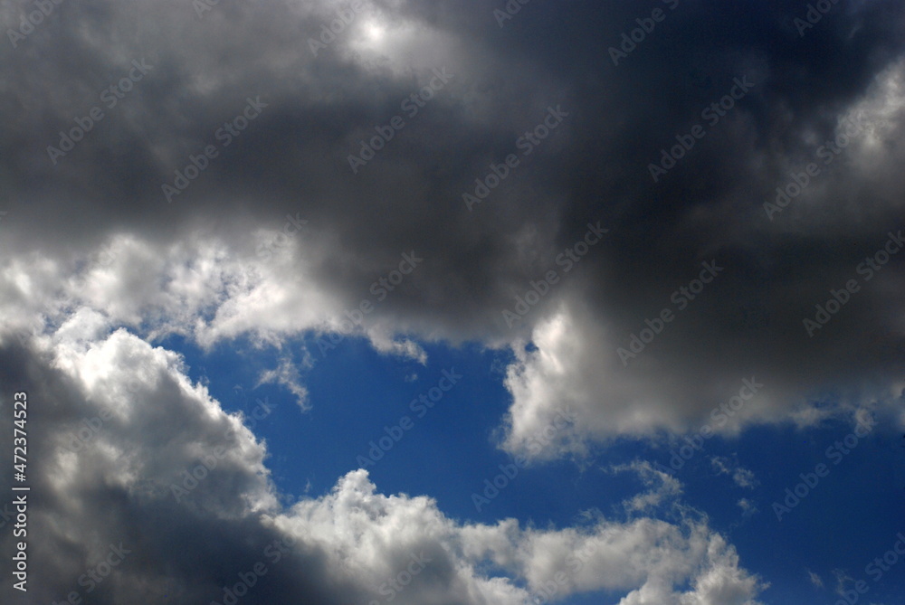 A large white-gray cloud covers the sky. A large white-gray cloud occupies the blue sky. The sun illuminates it from the top left, so that the bottom of the cloud is dark.