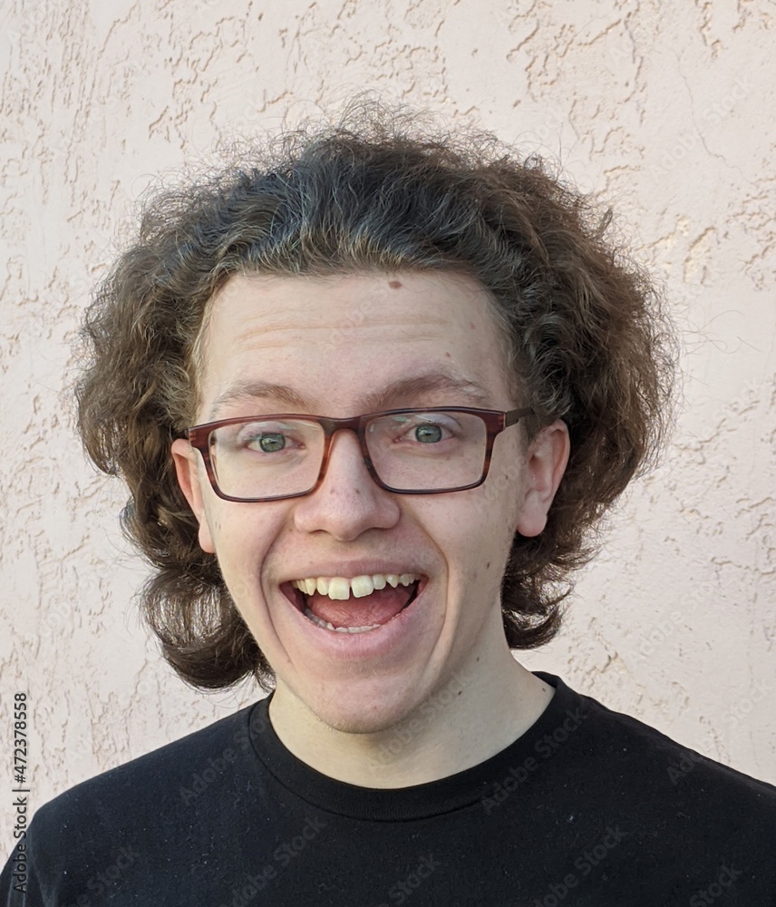 Portrait Of Smiling Teenage Boy With Curly Hair And Glasses Against Wall  Stock Photo | Adobe Stock