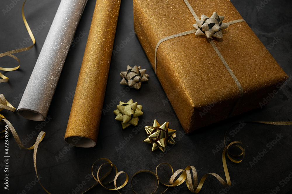 gift wrapping. wrapped golden present with wrapping paper rolls and  accessories on black stone background Stock Photo | Adobe Stock