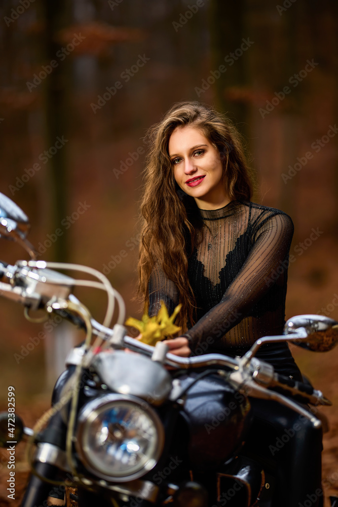 A beautiful woman with long hair on a chopper motorcycle in autumn landscape.