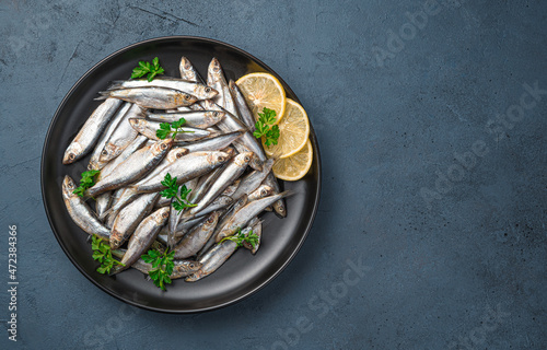A plate full of sardines with lemon and parsley on a dark blue background. Top view, copy space. Sea fish.