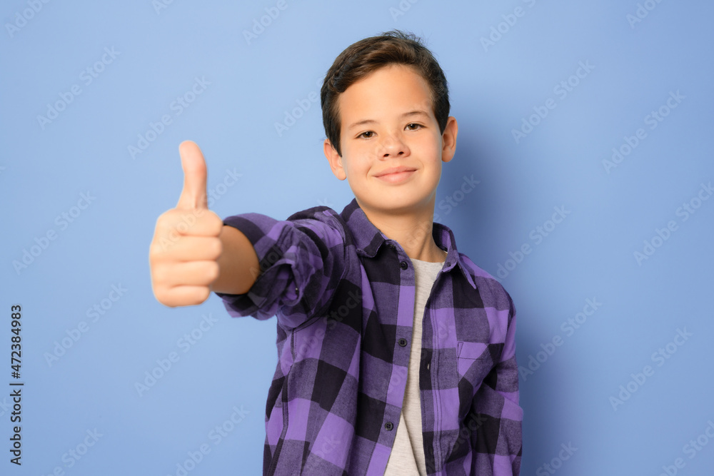 Smiling boy wearing plaid shirt showing thumb up isolated over purple background. Smiling boy wearing plaid shirt showing thumb up isolated over purple background.