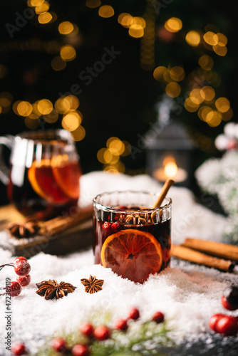 Cozy atmosphere with glass of Mulled wine, Christmas winter alcohol drink decorated by snow and christmas lights