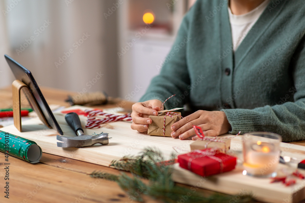 winter holidays and hobby concept - close up of woman with tablet pc computer packing christmas gift or making advent calendar at home winter holidays and hobby concept - close up of woman with tablet pc computer packing christmas gift or making advent calendar at home