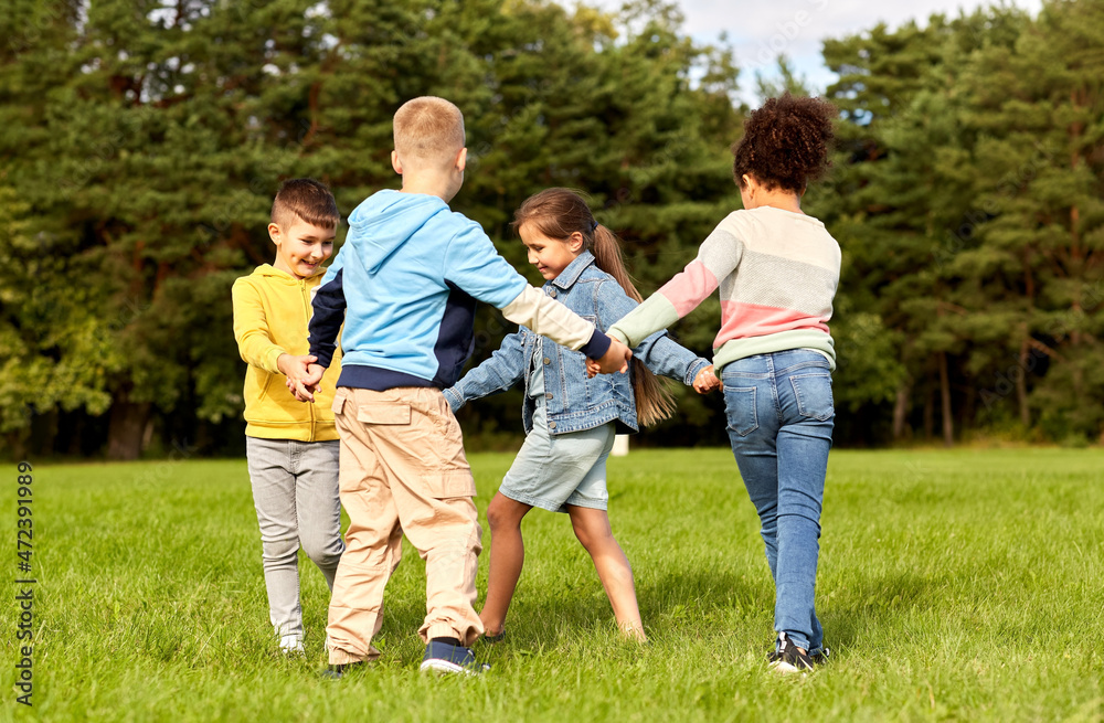 childhood, leisure and people concept - group of happy kids playing round dance at park childhood, leisure and people concept - group of happy kids playing round dance at park