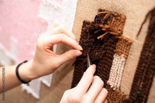 The process of making a tufting rug. Sewing scissors in female hands on the background of a handmade brown tank rug on sacking.