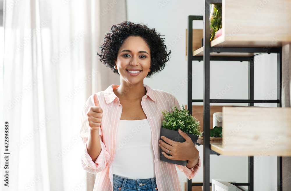 home improvement, decoration and people concept - happy smiling woman with flower or houseplant at shelf showing thumbs up