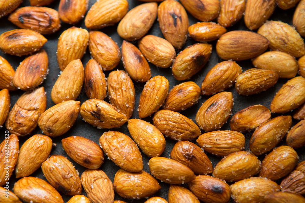 Filled frame background wallpaper shot of a bunch of crunchy roasted almonds with sea salt on a black background Filled frame background wallpaper shot of a bunch of crunchy roasted almonds with sea salt on a black background
