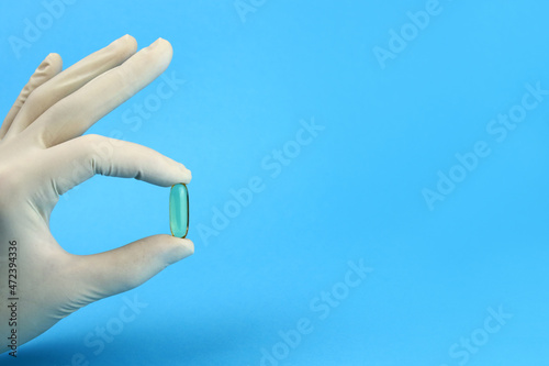 hand in a medical latex glove holds an omega 3 capsule. Space for text