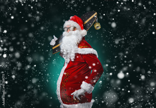 Waist up portrait of cool rock Santa with skateboard over dark background with snow falling, copy space
