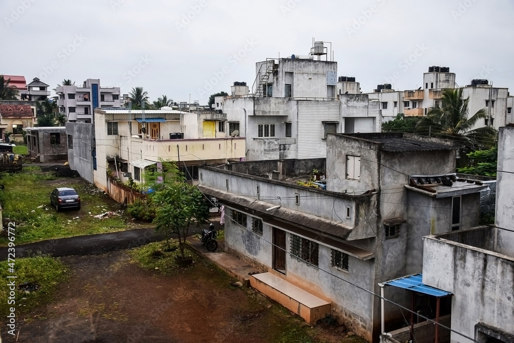 Obraz premium Roof top view of residential group housing , apartment and bungalows in the urban area, picture captured during rainy season with dark clouds. Parked vehicles outside of the houses at Kolhapur, India.