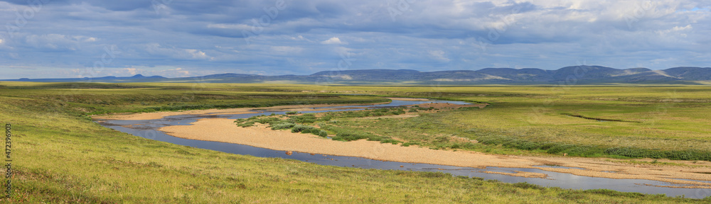 Wide panorama of a meandering river in the tundra in the Arctic. Summer season in the tundra. Picturesque northern nature of polar Siberia and Chukotka. Travel and hikes to the extreme North of Russia