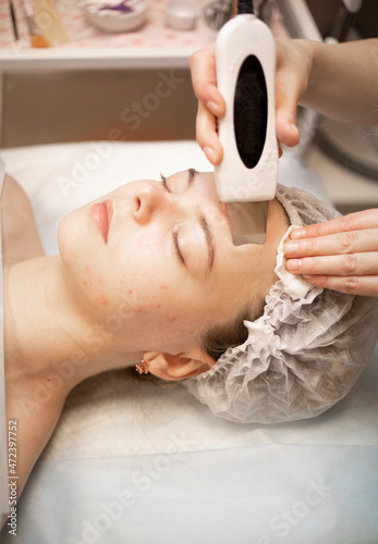 cleansing the problem skin of the girl's face with an ultrasound device, in the beautician's office. Doctor in work environment, reception, problem skin care
