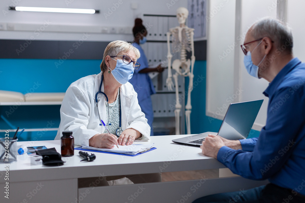Woman doctor with face mask taking notes on papers at medical consultation with man. Physician signing clipboard files for healthcare treatment and medicine during covid 19 pandemic