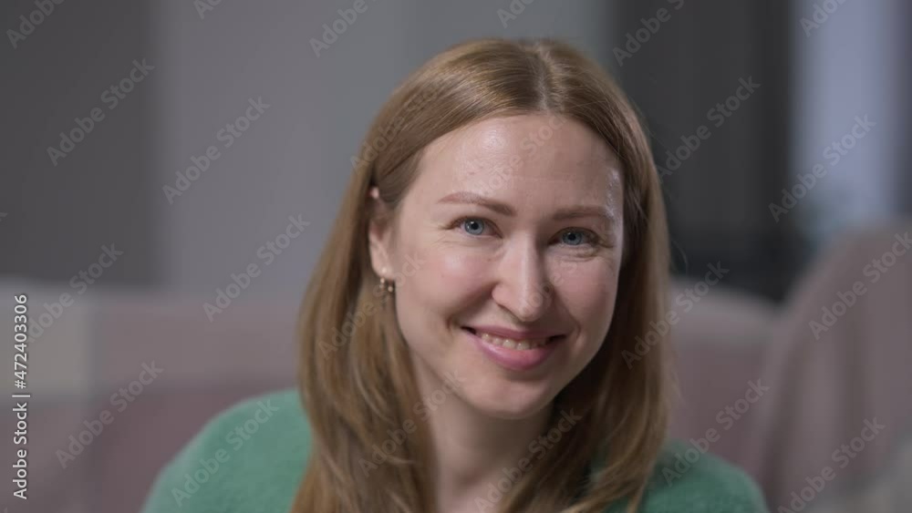 Portrait of charming slim beautiful Caucasian brunette woman with grey eyes posing in slow motion indoors. Happy cheerful lady looking at camera with toothy smile sitting at home in comfort Portrait of charming slim beautiful Caucasian brunette woman with grey eyes posing in slow motion indoors. Happy cheerful lady looking at camera with toothy smile sitting at home in comfort