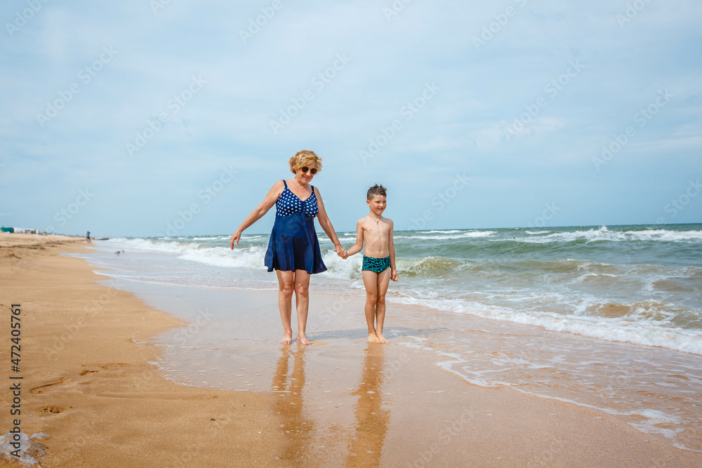 A grandmother is playing with her grandson on the beach when the wave crashes on their feet.