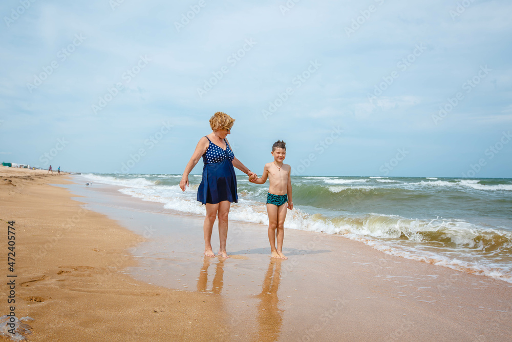 A grandmother is playing with her grandson on the beach when the wave crashes on their feet. A grandmother is playing with her grandson on the beach when the wave crashes on their feet.
