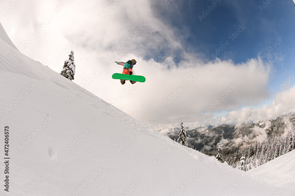 snowboarder performs masterful jump in the air over snowy mountain slope
