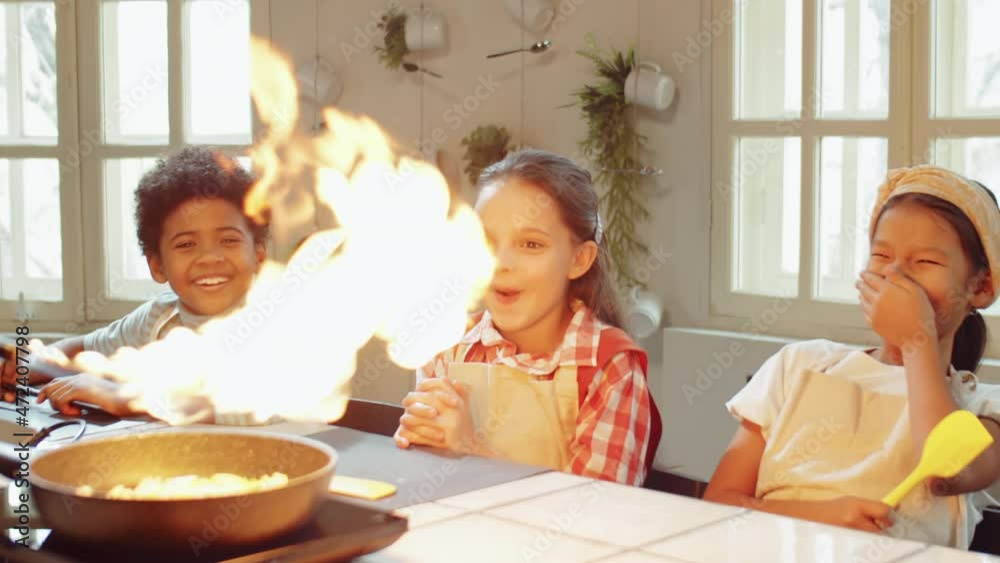 Amazed multiethnic children watching how chef flambeing food in skillet during cooking masterclass Amazed multiethnic children watching how chef flambeing food in skillet during cooking masterclass