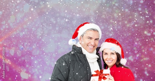 Composition of happy couple with christmas gift against bokeh and snowy background, copy space