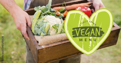 Midsection of man holding crate full of fresh vegetables with vegan menu in heart shape symbol