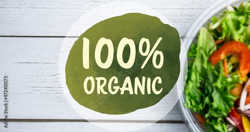 Overhead view of 100 percent organic symbol text by fresh salad in bowl on white table