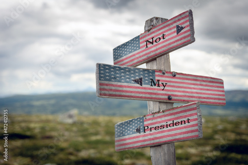not my president text quote on wooden signpost with the american flag outdoors in nature.