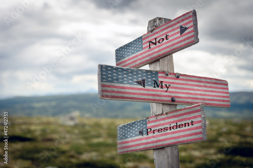 not my president text quote on wooden signpost with the american flag outdoors in nature. photo