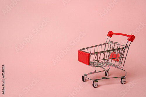 Metallic shopping cart trolley on pink color background with copy space. Shopping symbol. Concept of online shopping and commerce.