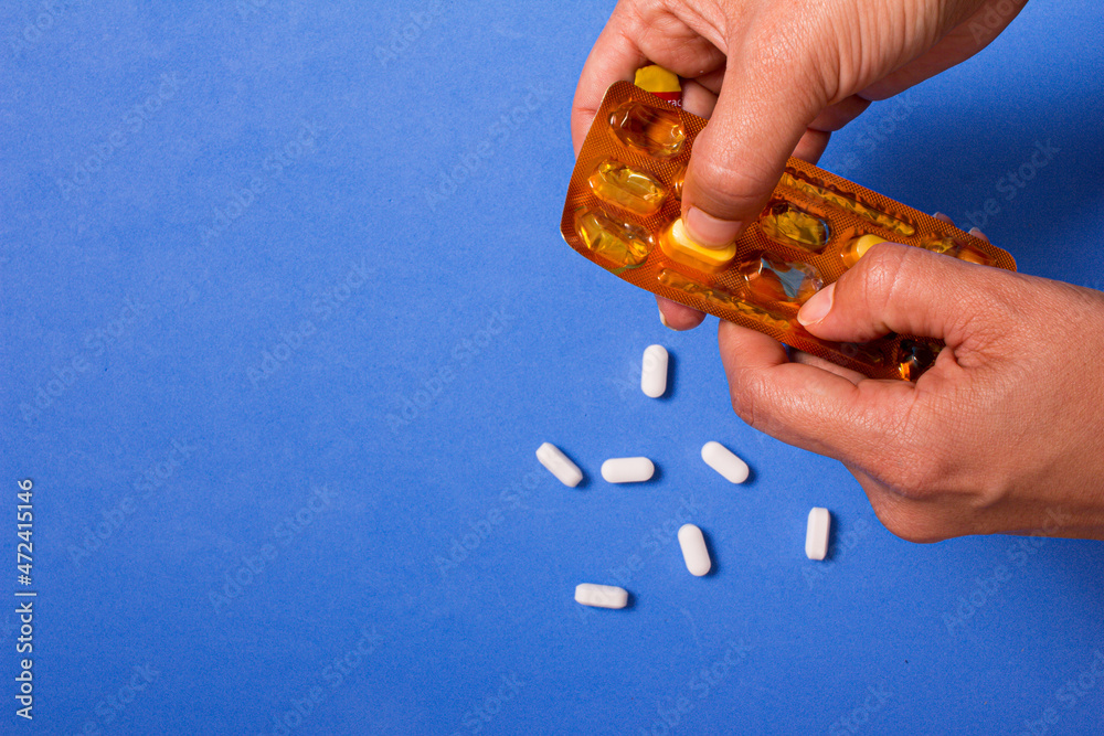 Hand holding white pills on blue background. Copy space. Hand holding white pills on blue background. Copy space.