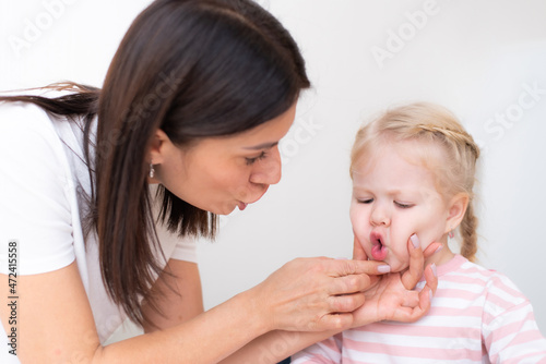 Woman speech therapist helps cute girl to learn correct pronunciation and literate speech