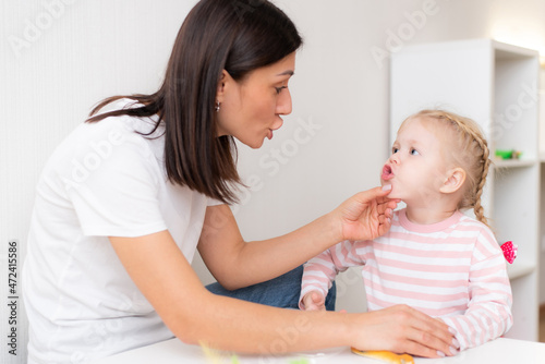 Woman speech therapist helps cute girl to learn correct pronunciation and literate speech