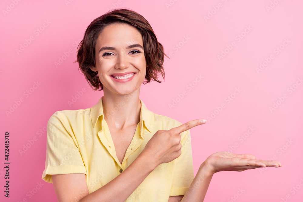 Photo of funny young brunette lady hold point empty space wear yellow t-shirt isolated on pink color background Photo of funny young brunette lady hold point empty space wear yellow t-shirt isolated on pink color background