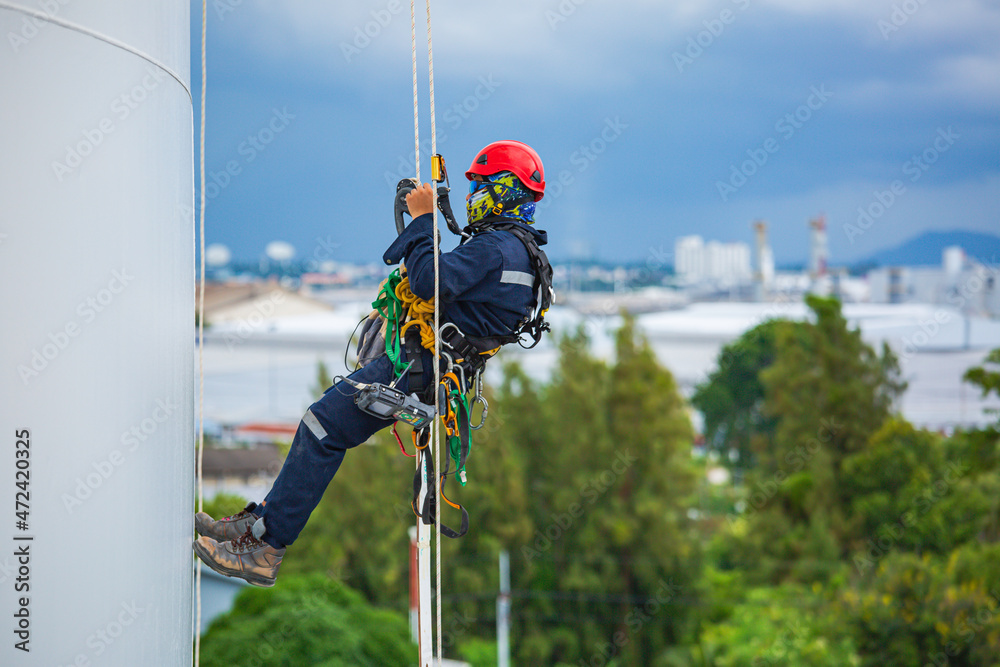 Close-up male workers control equipment rope down tank rope access background cloud storm. Close-up male workers control equipment rope down tank rope access background cloud storm.